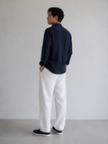 Man wearing a navy shirt and white pants standing against a plain background