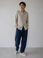 Man wearing a beige shirt and blue pants against a plain background