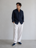 Man wearing a navy shirt and white pants against a plain background