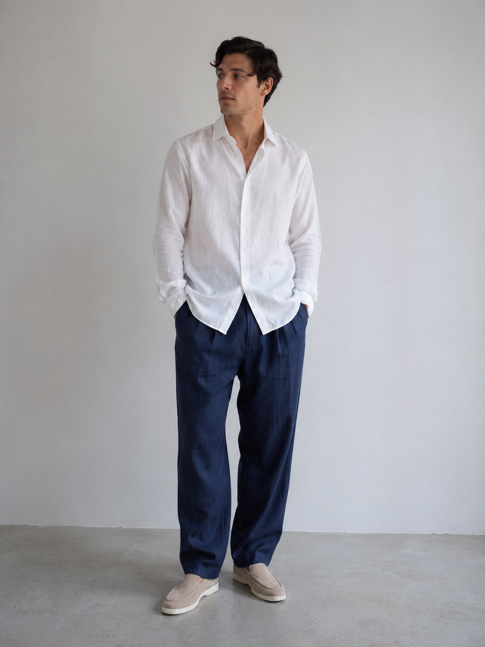 Man wearing a white shirt and navy pants against a plain background