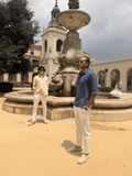 Two men standing in front of a fountain in an outdoor setting with a building and trees in the background.
