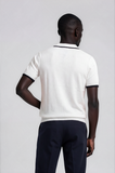 Person wearing a white polo shirt with black trim on a plain background