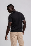 Man wearing a black polo shirt with white trim on a plain background