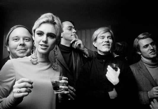 Andy Warhol wearing a black turtleneck at a social gathering, surrounded by a group of people, 1960s black and white photography