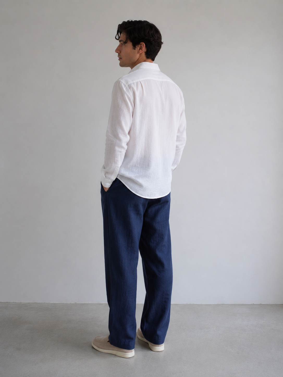 Man wearing a white shirt and navy pants against a plain background