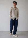 Man wearing a beige shirt and blue pants against a plain background
