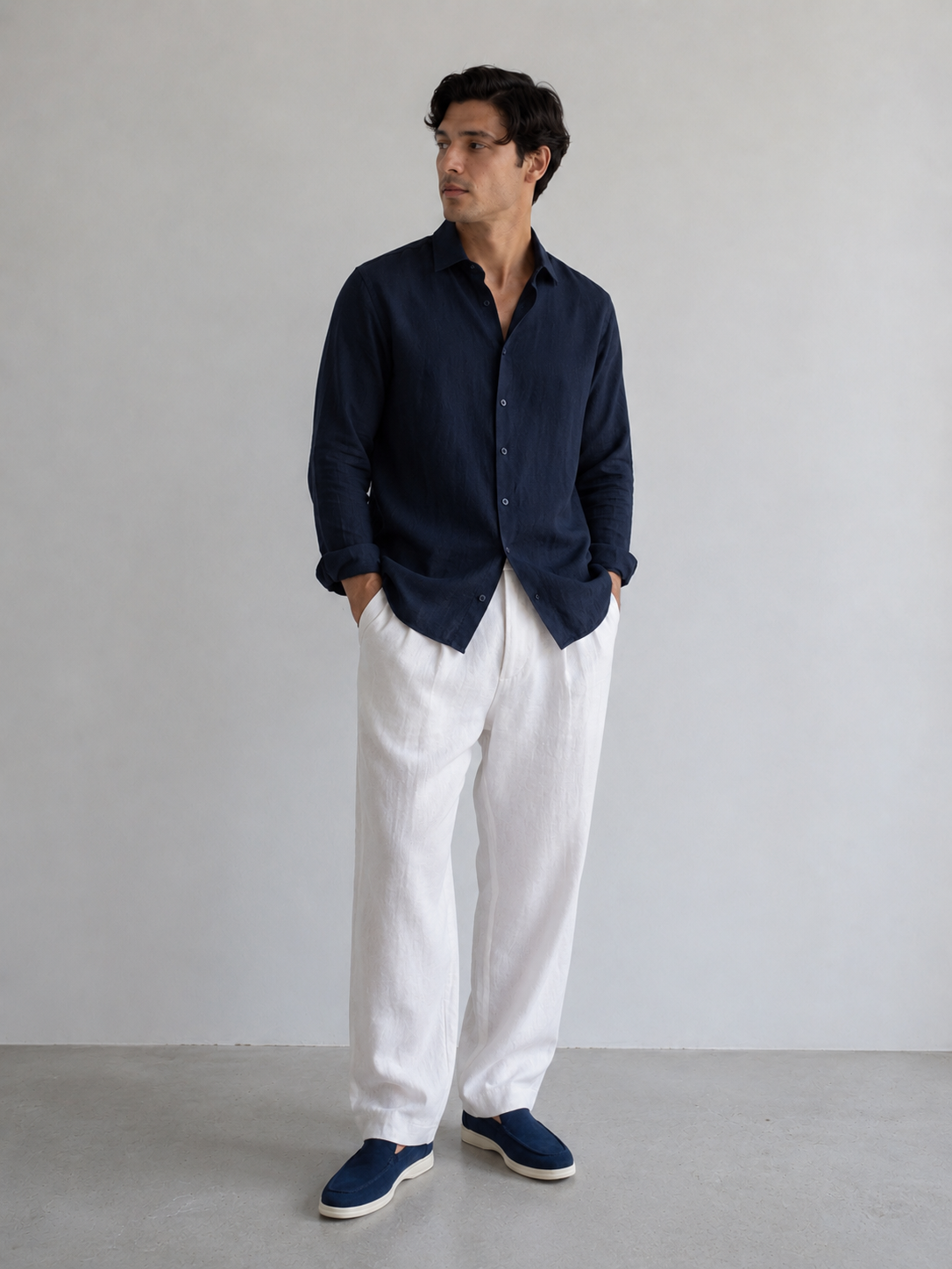 Man wearing a navy shirt and white pants against a plain background