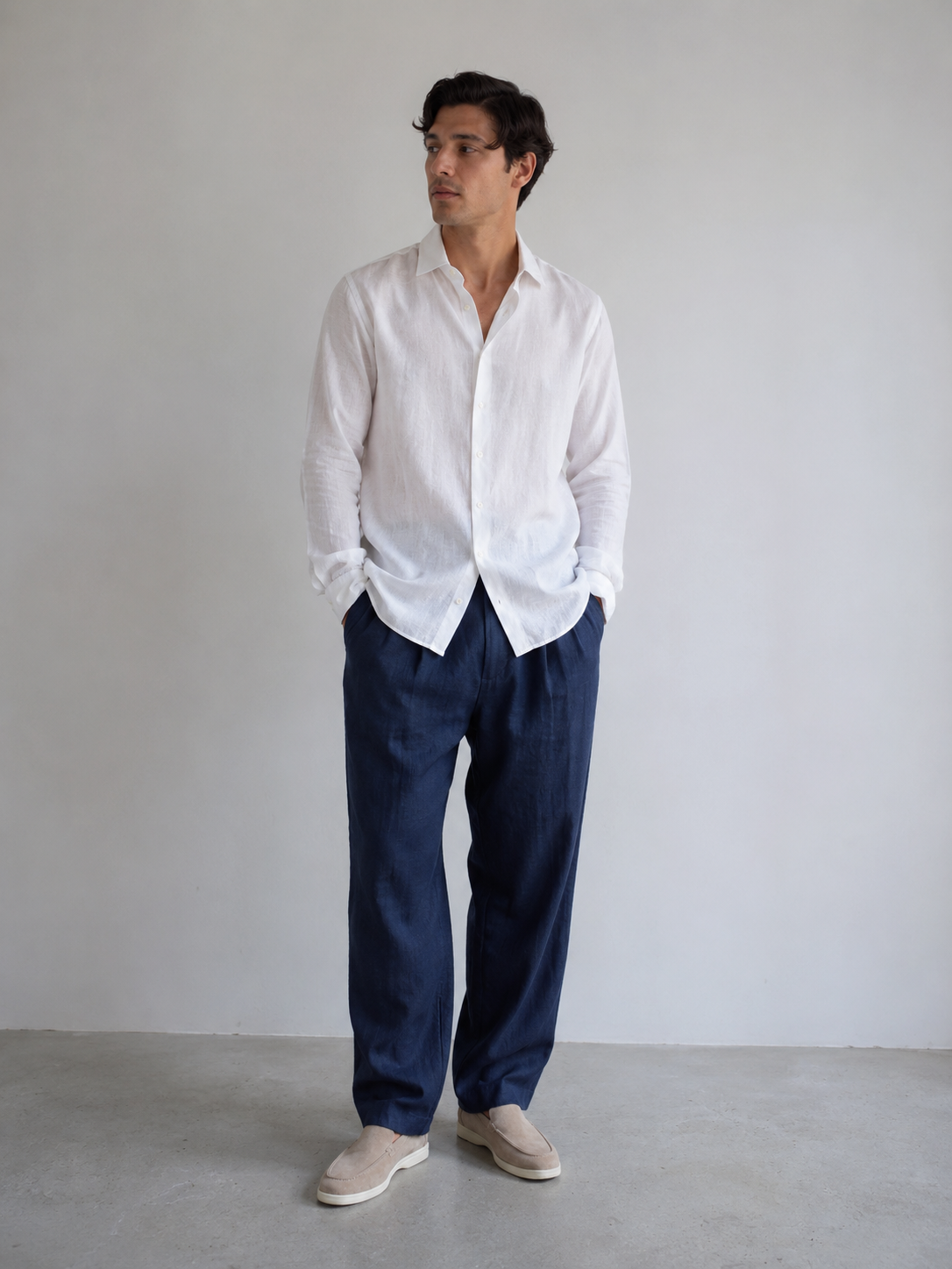 Man wearing a white shirt and navy pants against a plain background